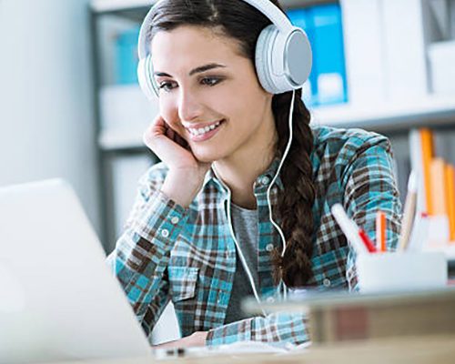Teenage smiling girl using a laptop and wearing headphones, technology and leisure concept